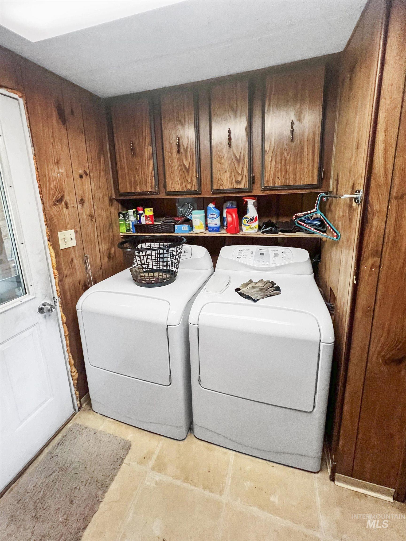 Laundry area with wood walls, washer and clothes dryer, cabinet space, and light tile patterned flooring