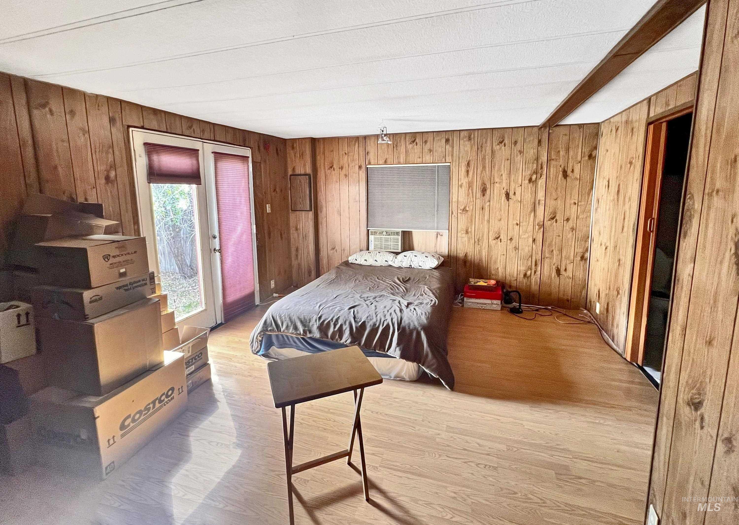 Bedroom with wooden walls, light wood-type flooring, access to exterior, and cooling unit