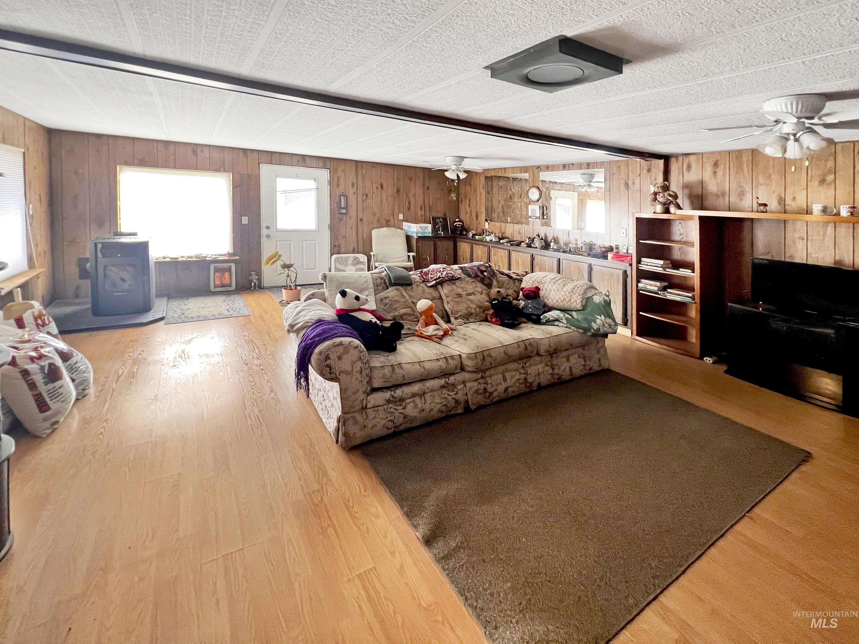 Living area featuring a ceiling fan, plenty of natural light, light wood-style flooring, and wood walls