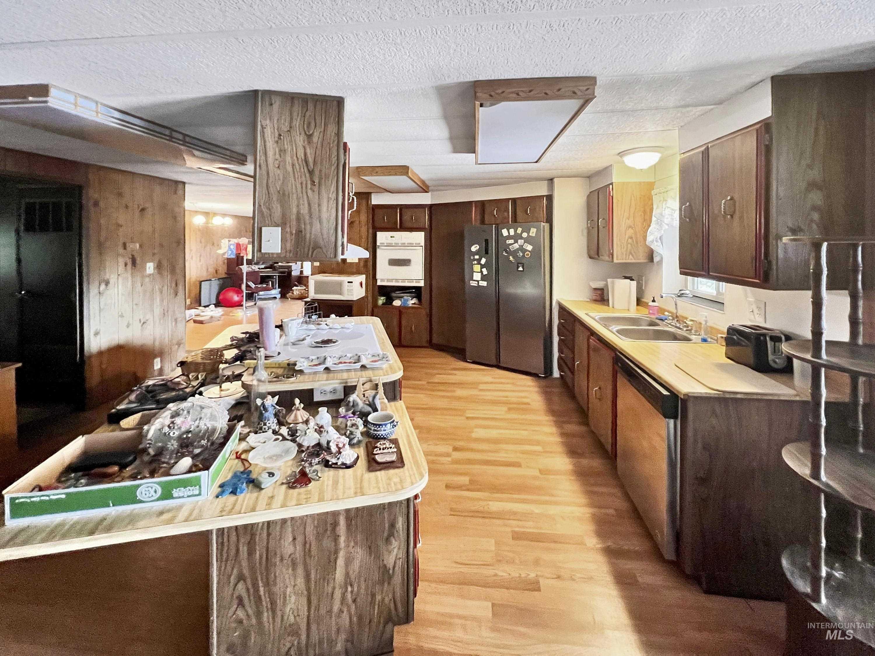Kitchen featuring freestanding refrigerator, light wood finished floors, light countertops, dishwasher, and dark brown cabinetry