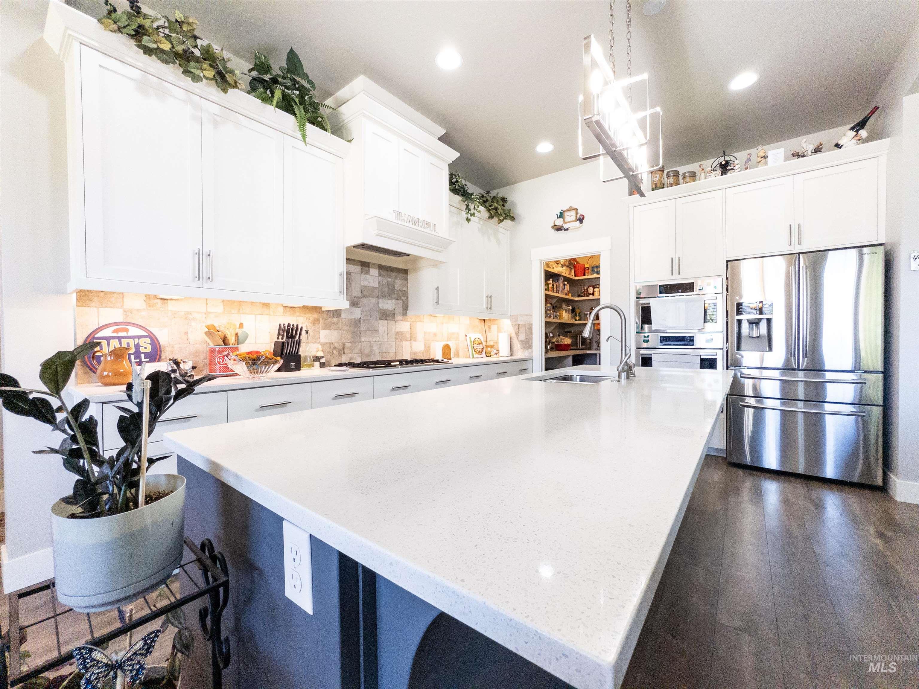 Kitchen featuring appliances with stainless steel finishes, white cabinets, tasteful backsplash, pendant lighting, and light stone counters