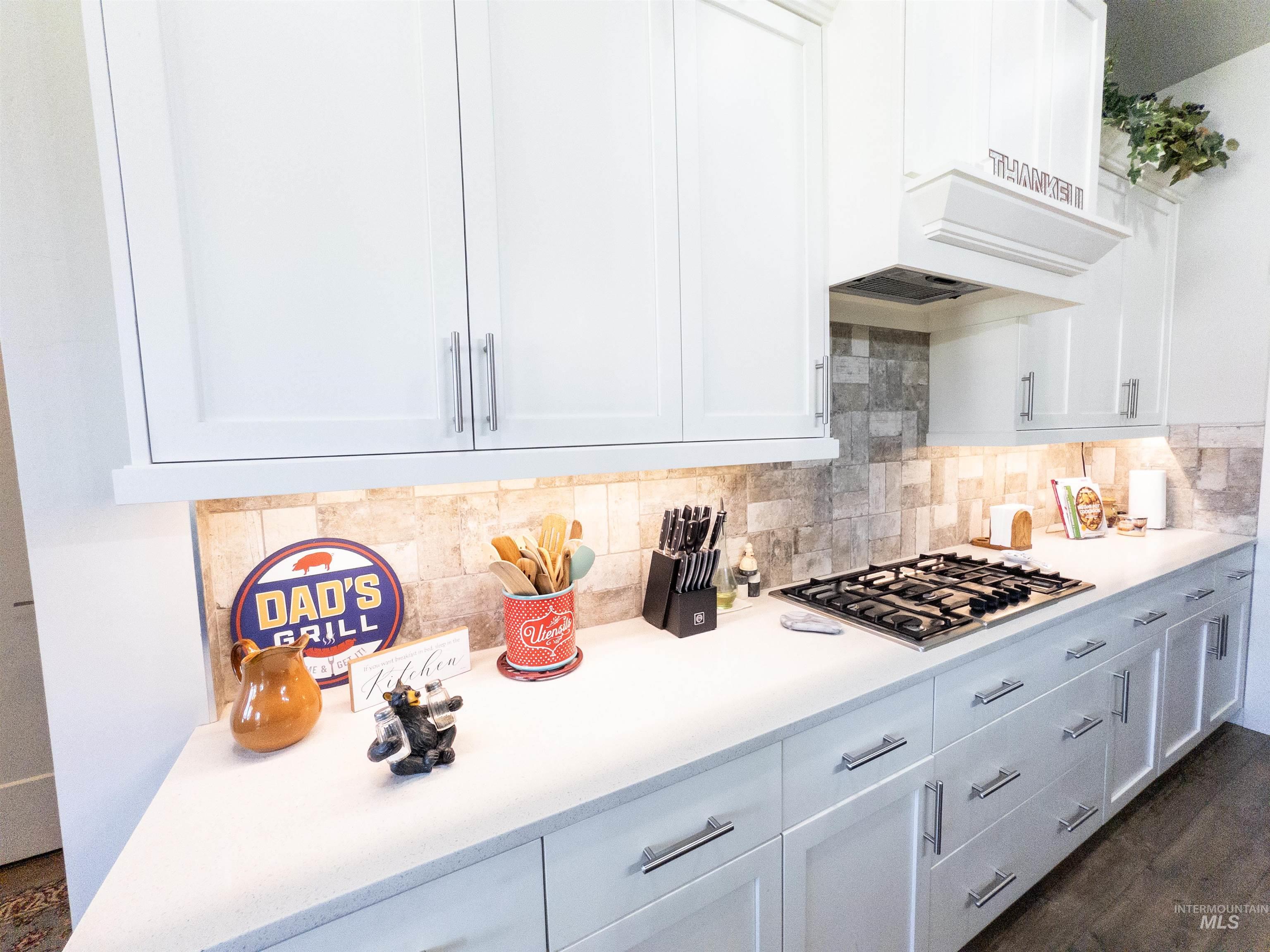 Kitchen with white cabinets, tasteful backsplash, stainless steel gas stovetop, and dark wood-style floors