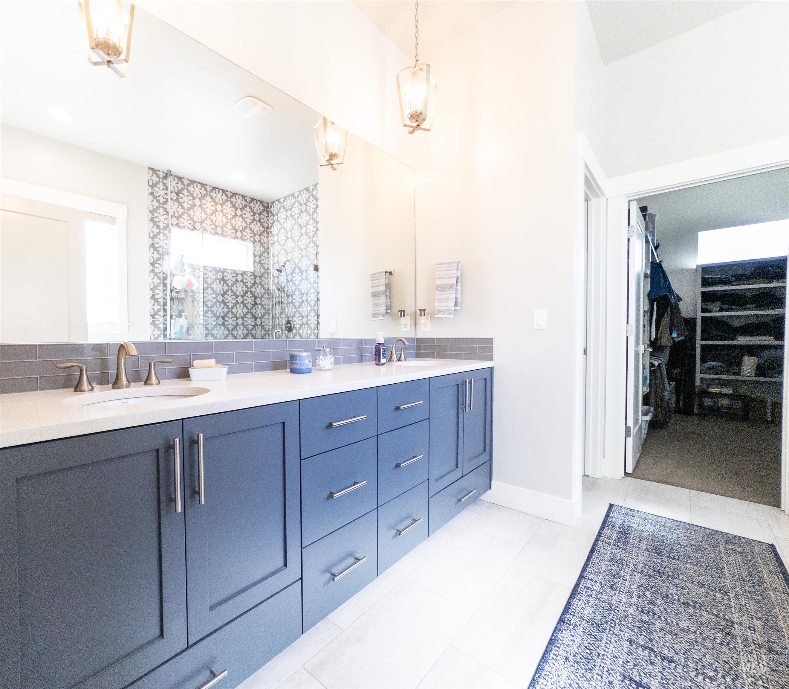 Bathroom featuring double vanity, a spacious closet, light tile patterned floors, and a tile shower