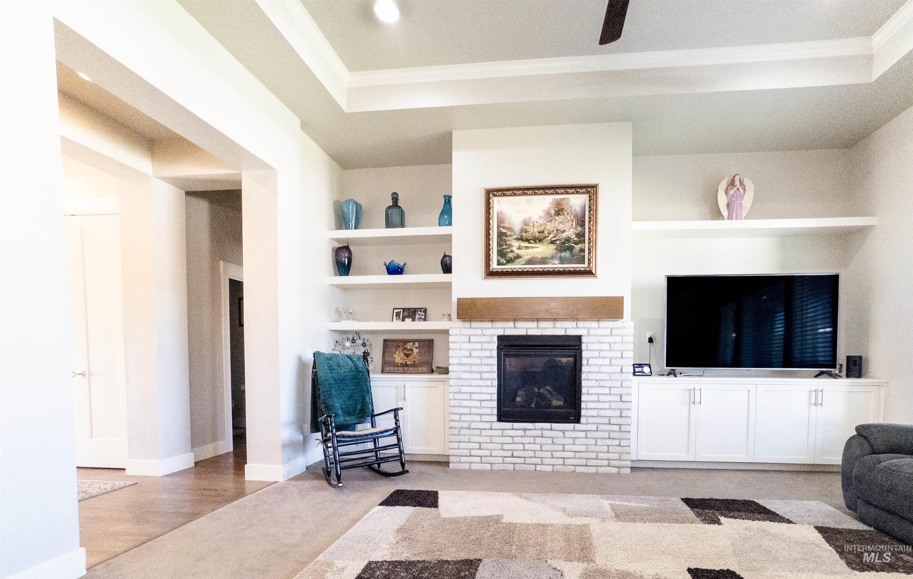 Living room with built in shelves, a fireplace, a tray ceiling, light carpet, and ornamental molding
