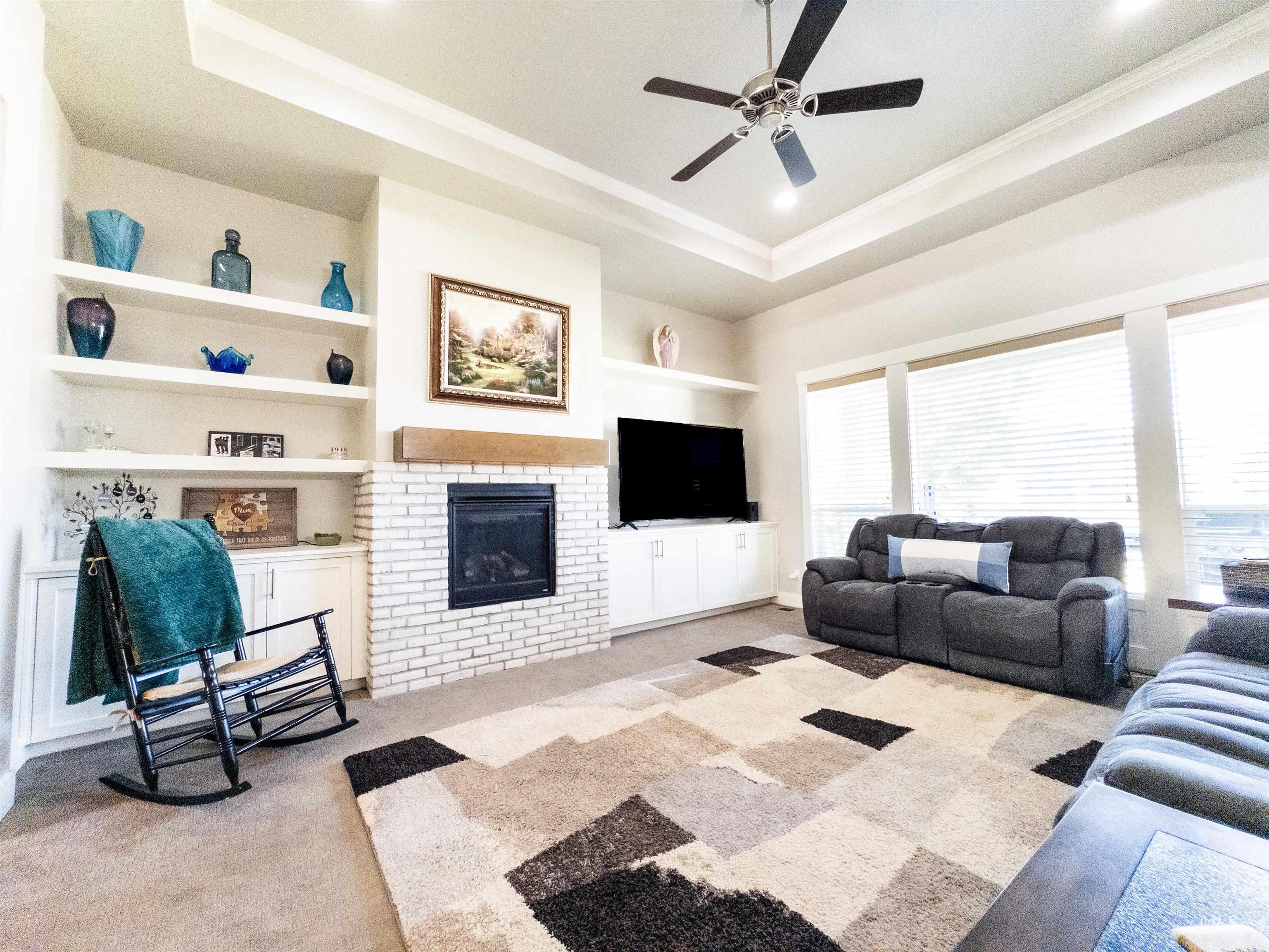 Living room with built in shelves, a tray ceiling, a fireplace, light carpet, and crown molding