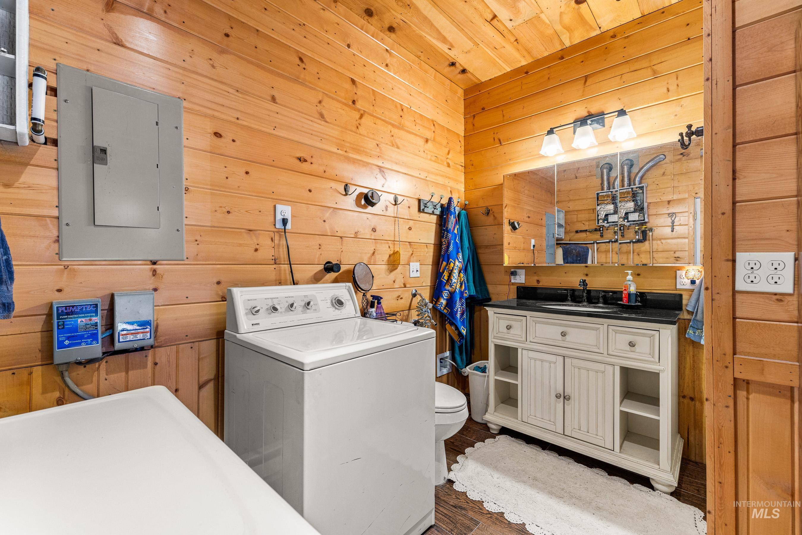 Laundry room featuring wood walls, washer / dryer, electric panel, wood finished floors, and wood ceiling