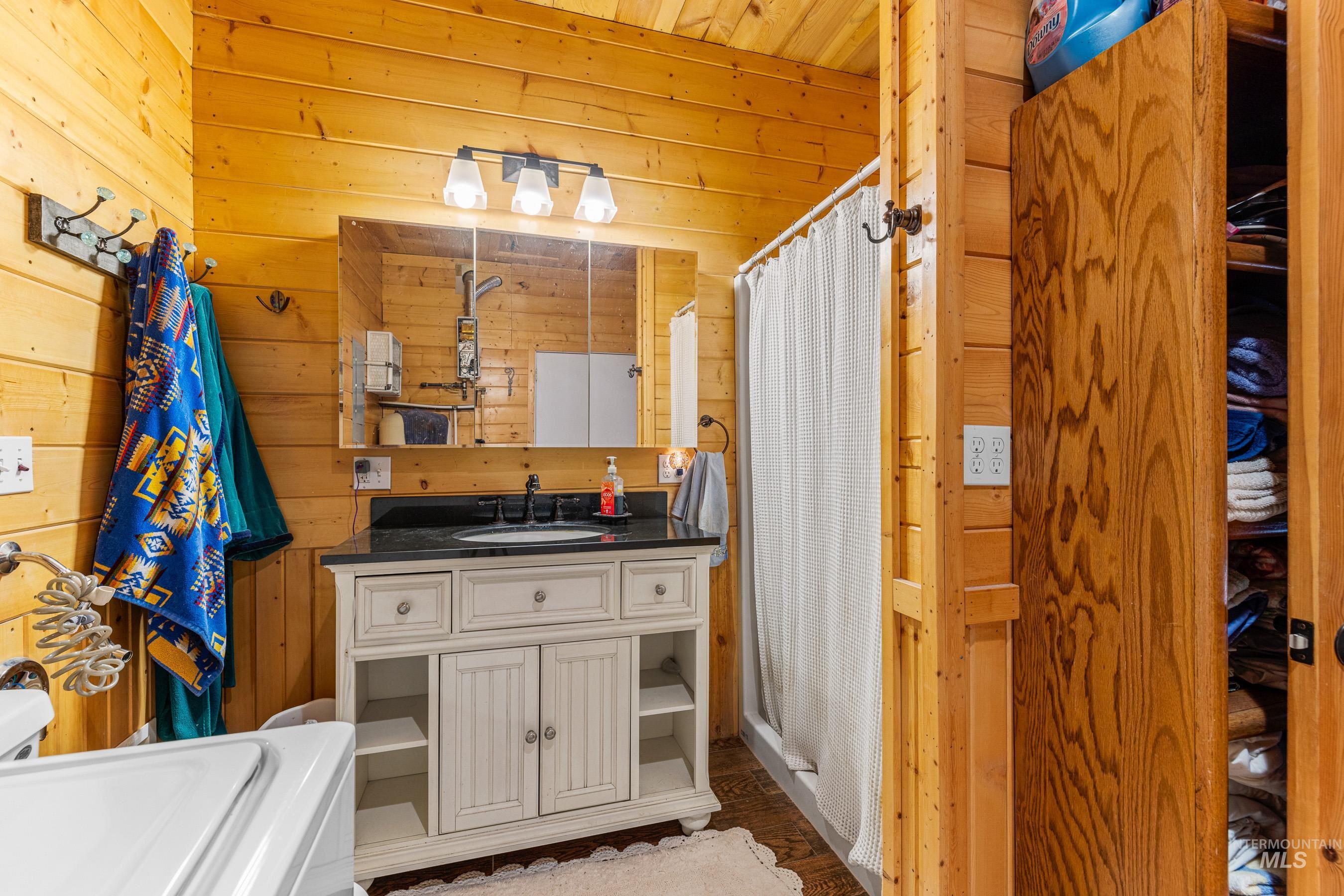 Bathroom with wooden walls, dark wood-style floors, vanity, washer / clothes dryer, and a shower with shower curtain