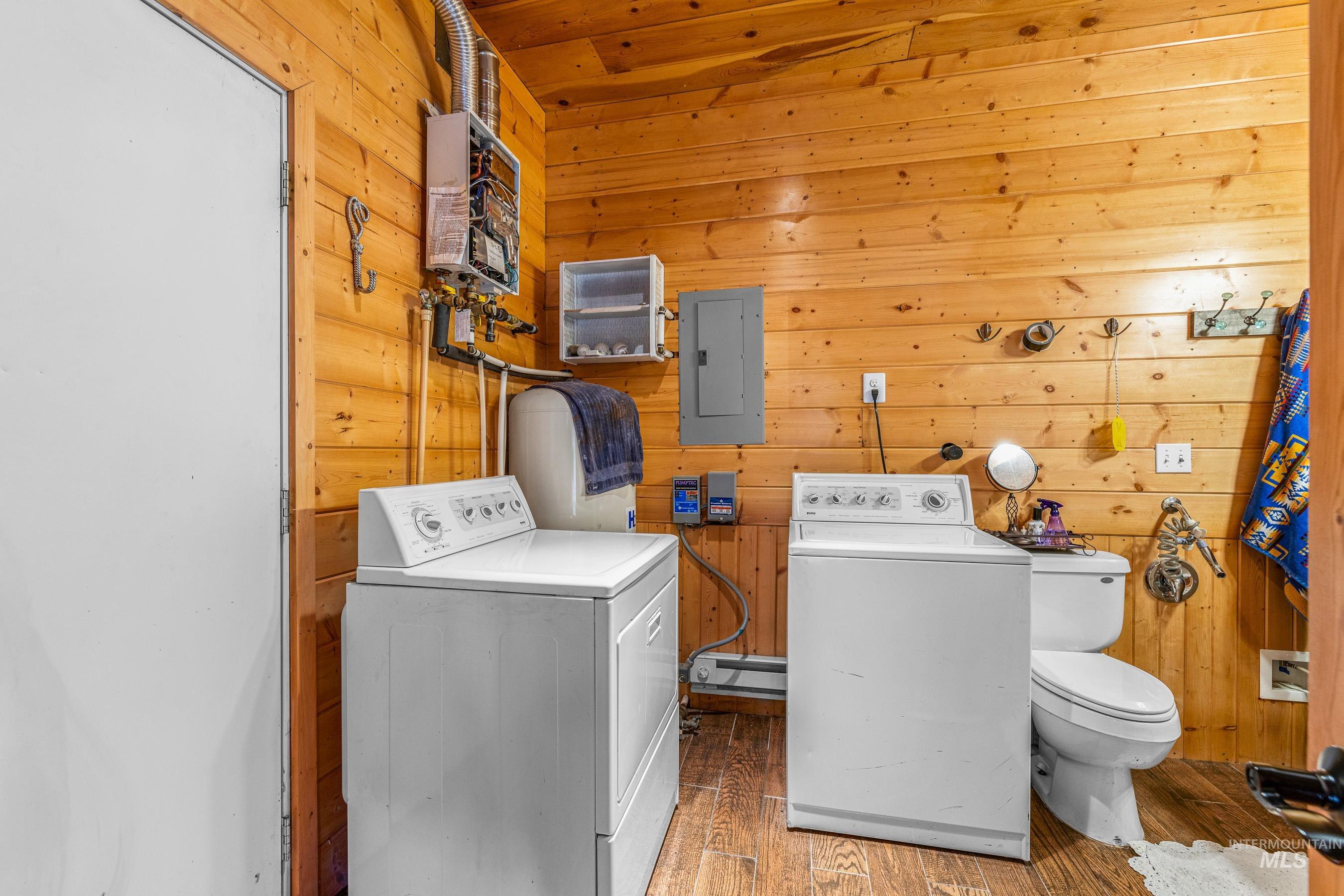 Laundry room with wooden walls, washer and dryer, wood finished floors, electric panel, and a baseboard heating unit