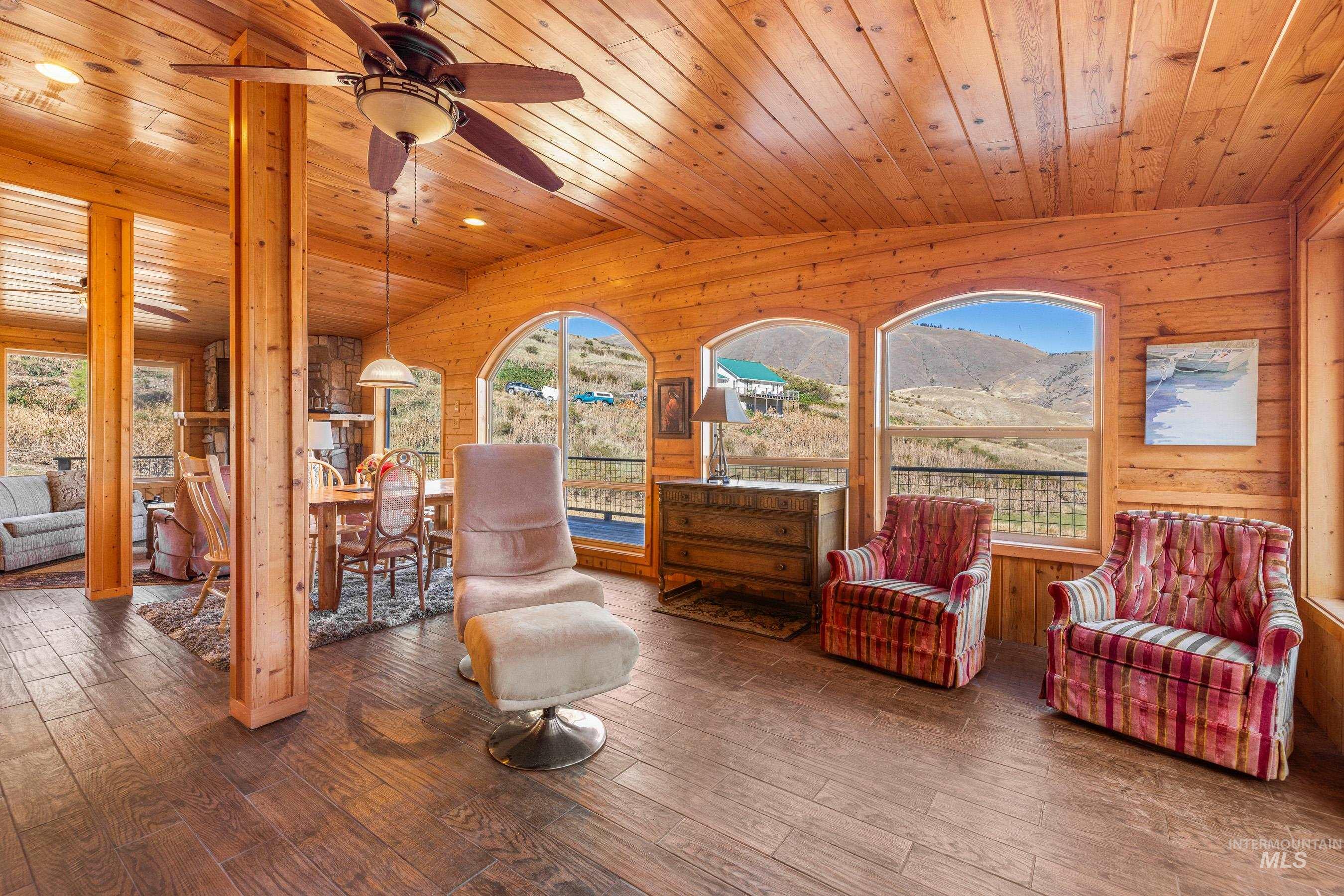 Sitting room with a mountain view, hardwood / wood-style floors, wood walls, lofted ceiling, and ceiling fan