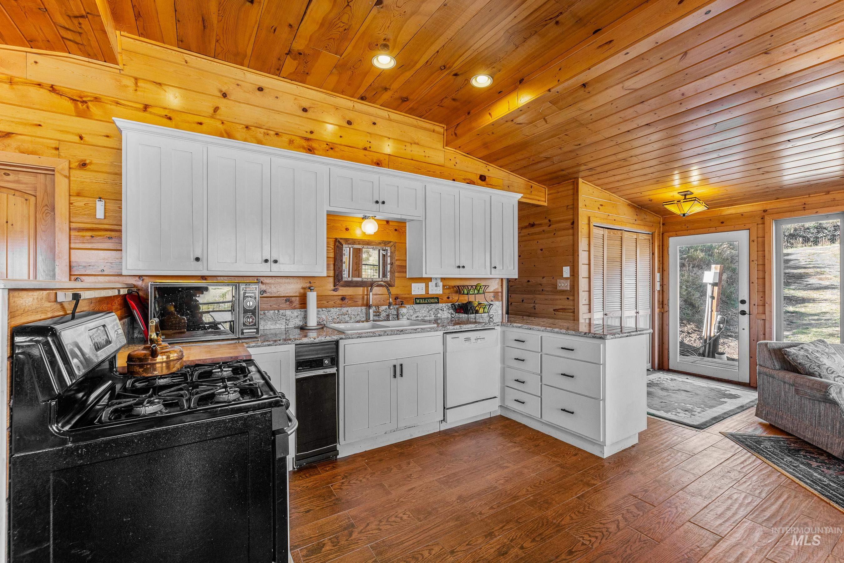 Kitchen featuring gas stove, white cabinets, dark wood-style floors, lofted ceiling, and wood walls