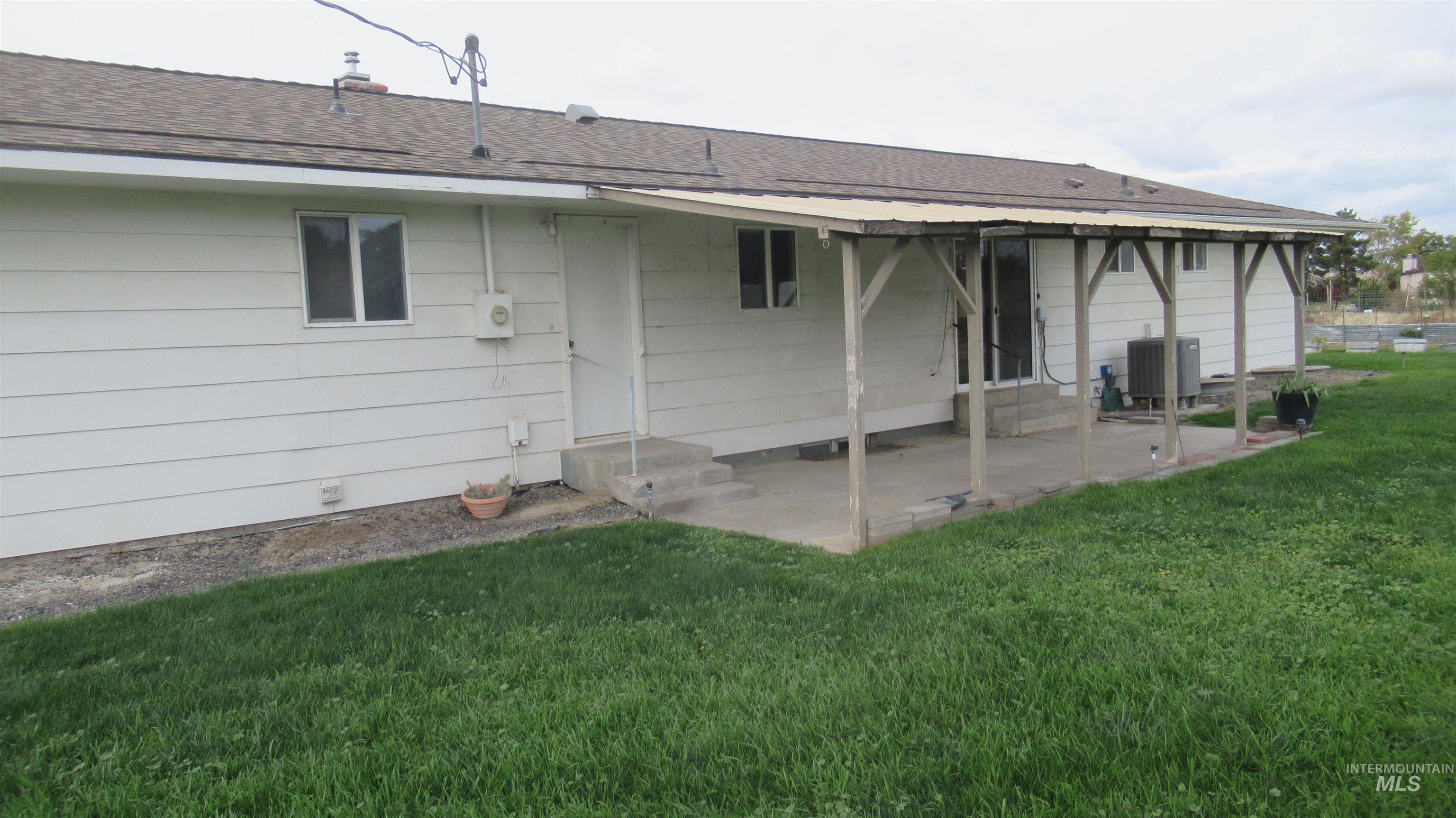 Rear view of property featuring entry steps, a lawn, a shingled roof, and a patio area