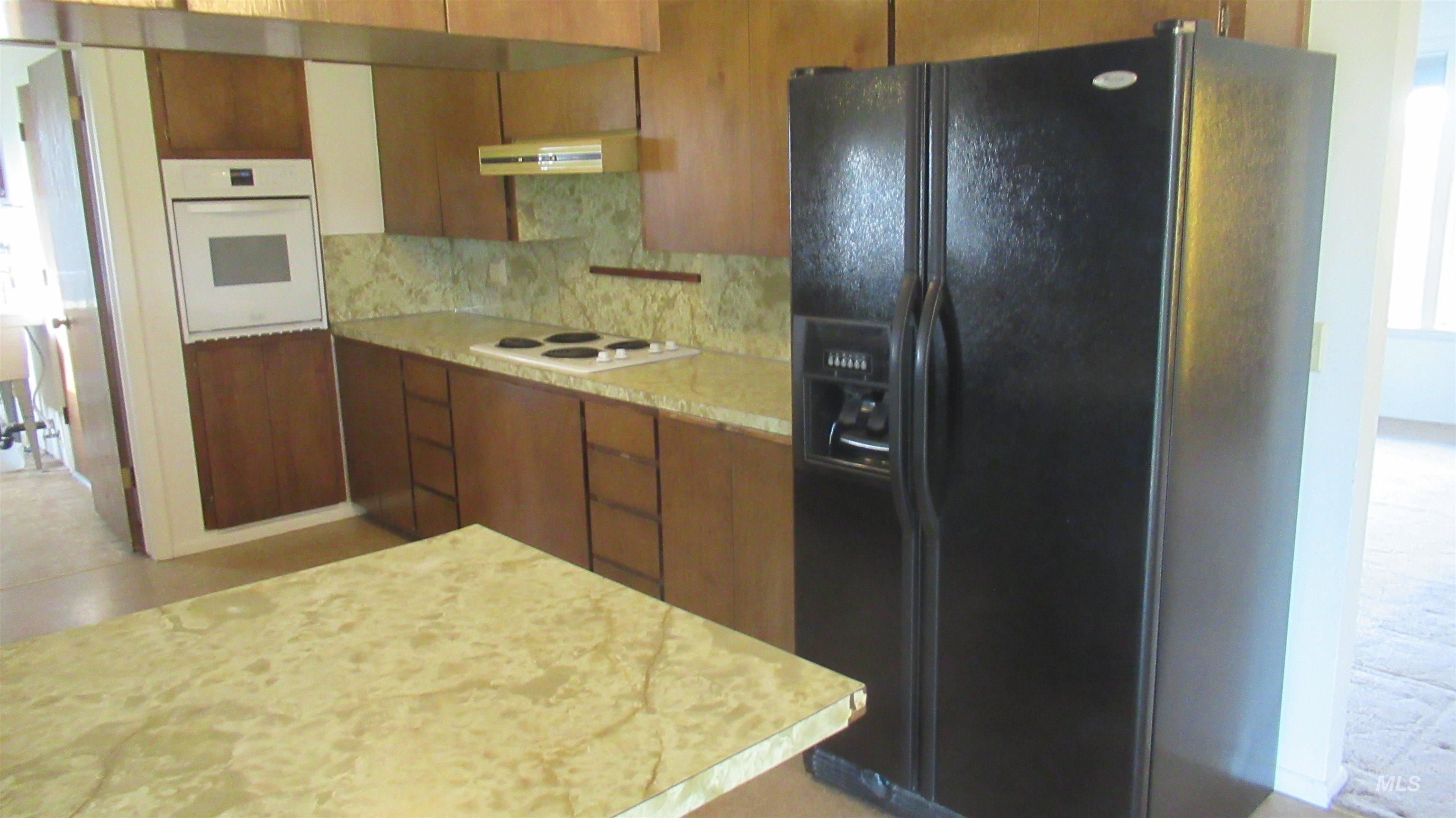 Kitchen with white appliances, light countertops, tasteful backsplash, exhaust hood, and brown cabinetry