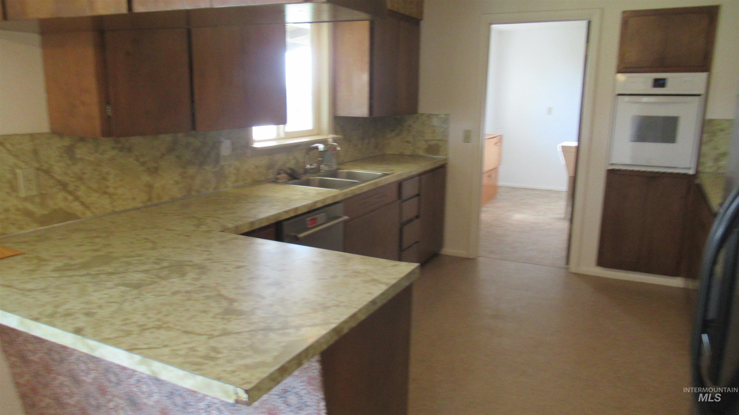 Kitchen with light countertops, stainless steel appliances, tasteful backsplash, brown cabinetry, and a peninsula