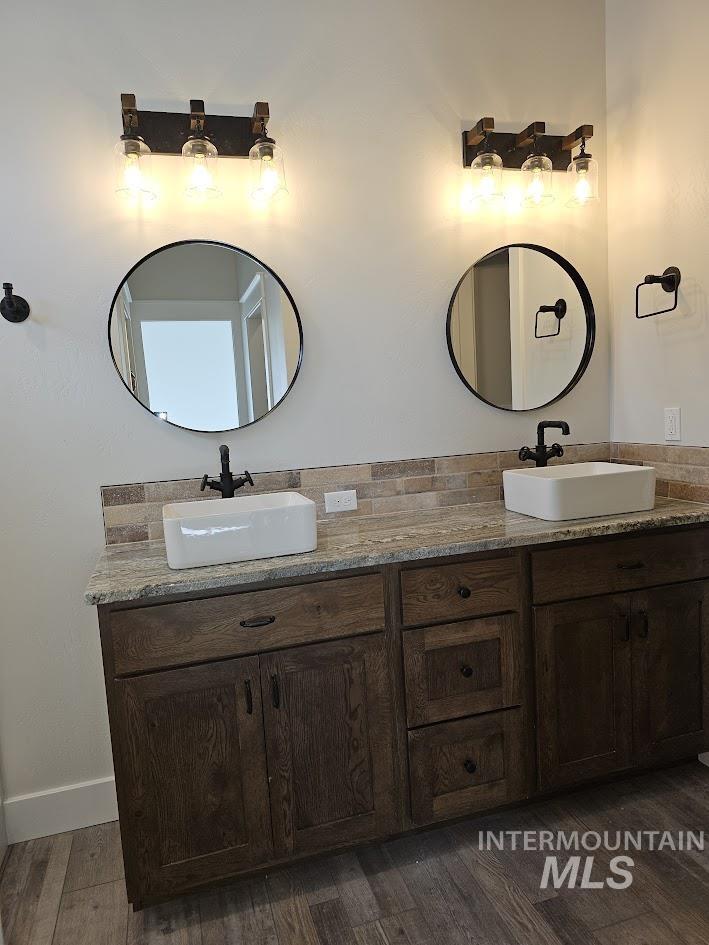 Bathroom featuring double vanity, dark wood-style floors, and tasteful backsplash