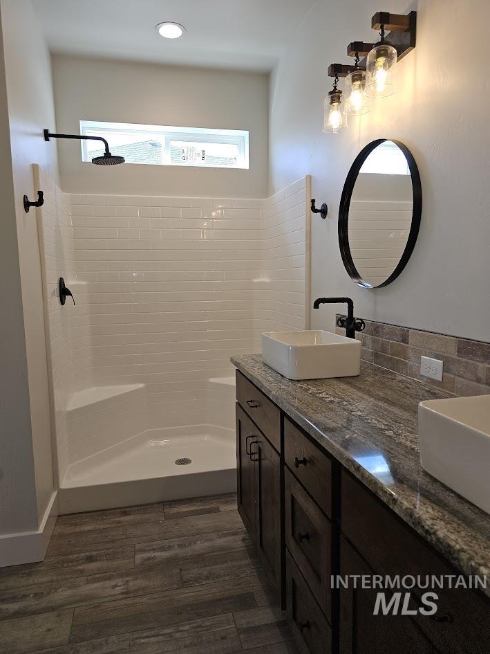 Bathroom with double vanity, a stall shower, and dark wood-style flooring