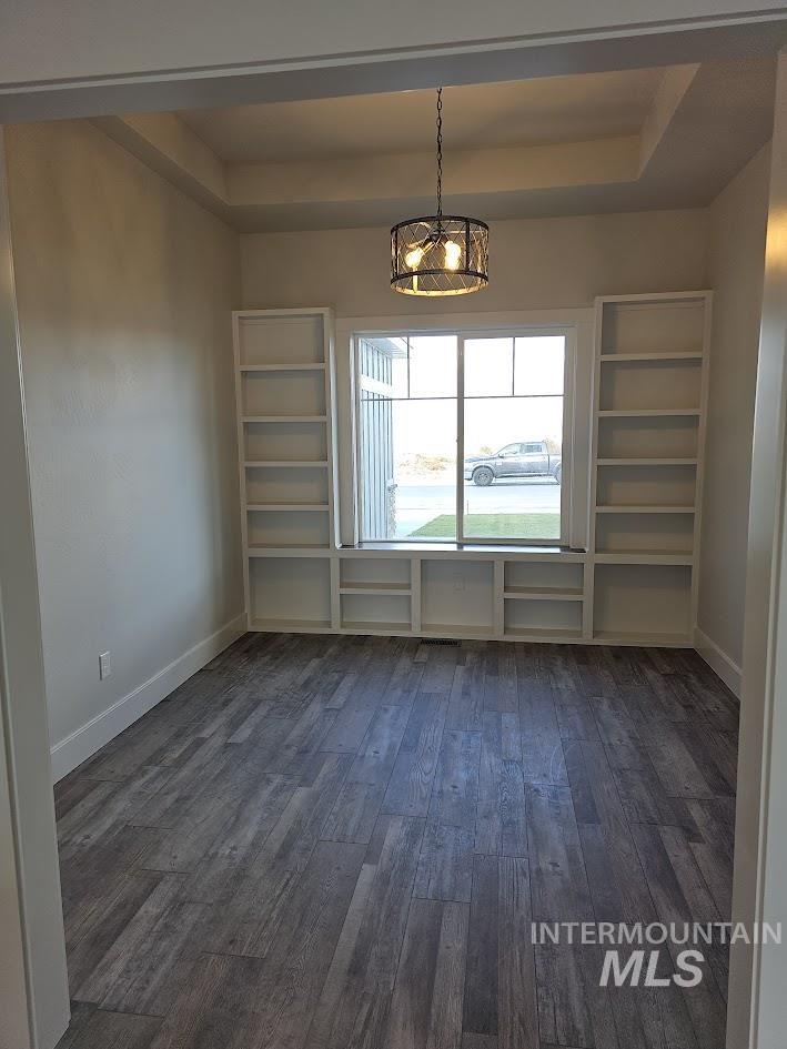 Unfurnished dining area with dark wood-style flooring, a tray ceiling, and a chandelier