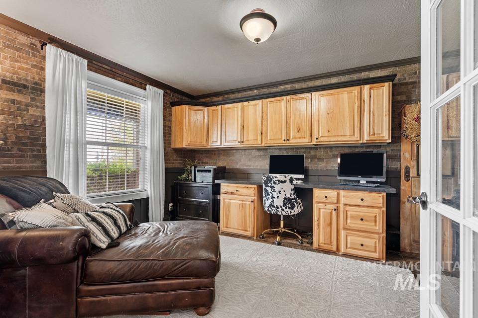 Home office featuring built in study area, brick wall, ornamental molding, and a textured ceiling