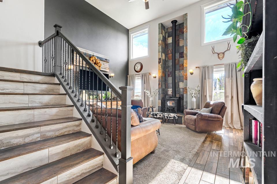 Living room featuring a wood stove, a towering ceiling, wood-type flooring, stairway, and ceiling fan