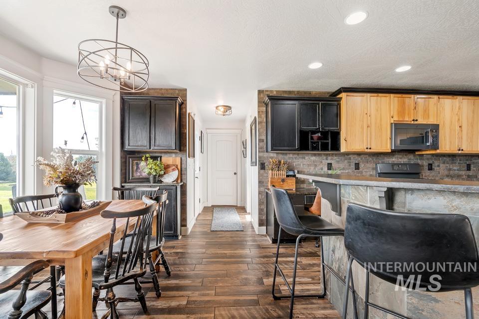 Kitchen with tasteful backsplash, black microwave, dark wood-style floors, decorative light fixtures, and a breakfast bar area