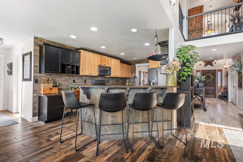 Kitchen with a breakfast bar, dark wood-style floors, dark stone countertops, backsplash, and stainless steel appliances