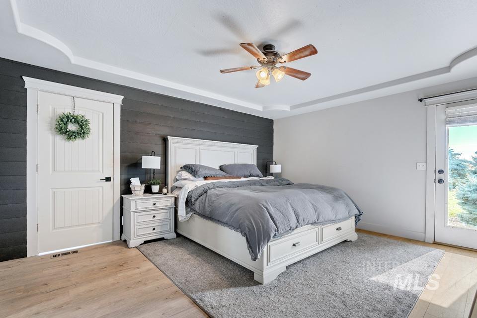 Bedroom with light wood-style floors, a ceiling fan, access to exterior, and a tray ceiling