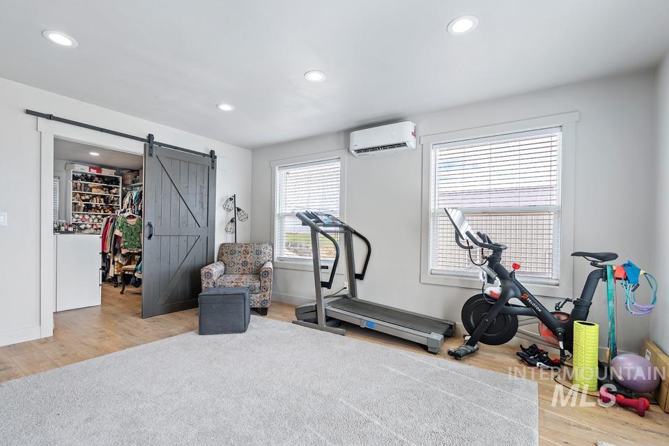 Exercise room with light wood-style floors, a barn door, recessed lighting, and an AC wall unit