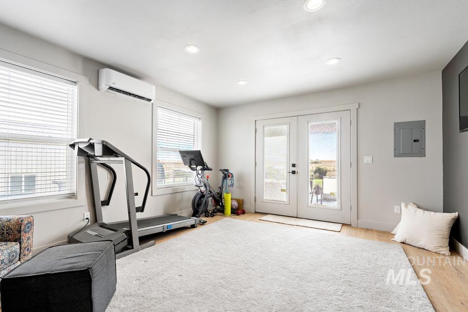 Exercise room featuring french doors, electric panel, light wood-style floors, recessed lighting, and a wall unit AC