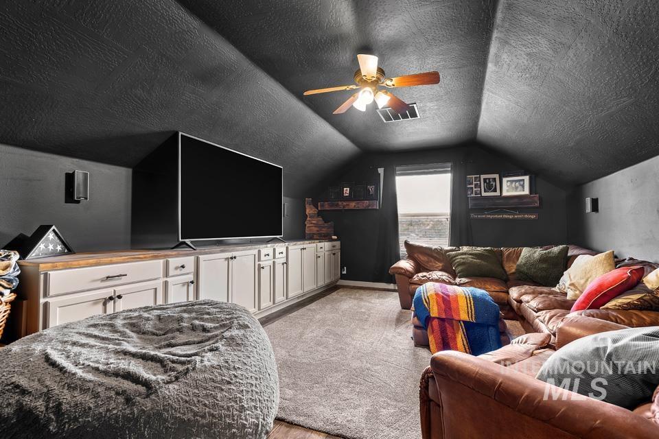 Home theater featuring a textured ceiling, a ceiling fan, vaulted ceiling, and light wood-style flooring