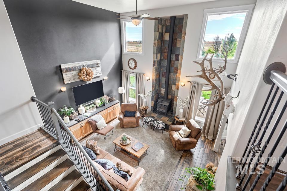Living area with a wood stove, dark wood-style flooring, a towering ceiling, stairway, and a ceiling fan