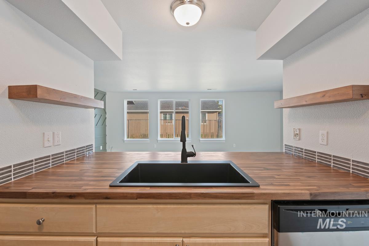 Kitchen with open shelves, a textured wall, wood counters, and stainless steel dishwasher