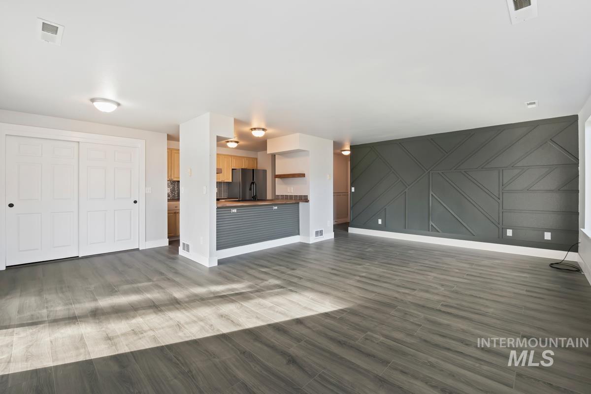 Unfurnished living room featuring dark wood-type flooring and a decorative wall