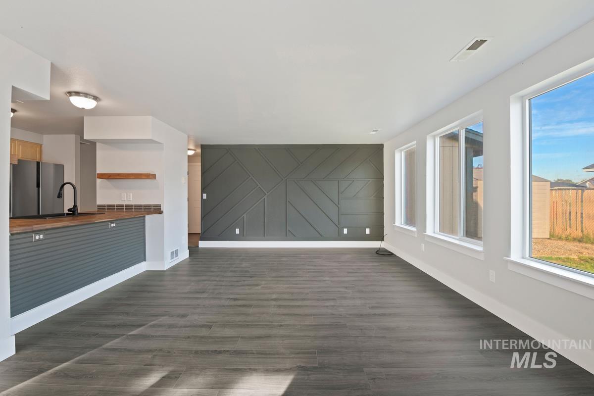 Unfurnished living room featuring plenty of natural light, dark wood-type flooring, and an accent wall