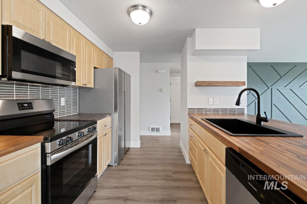 Kitchen with appliances with stainless steel finishes, backsplash, light wood-type flooring, and light brown cabinets