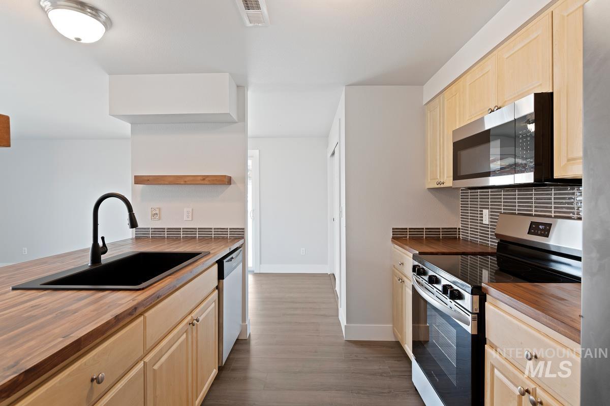 Kitchen with stainless steel appliances, light brown cabinetry, dark wood-style floors, and open shelves