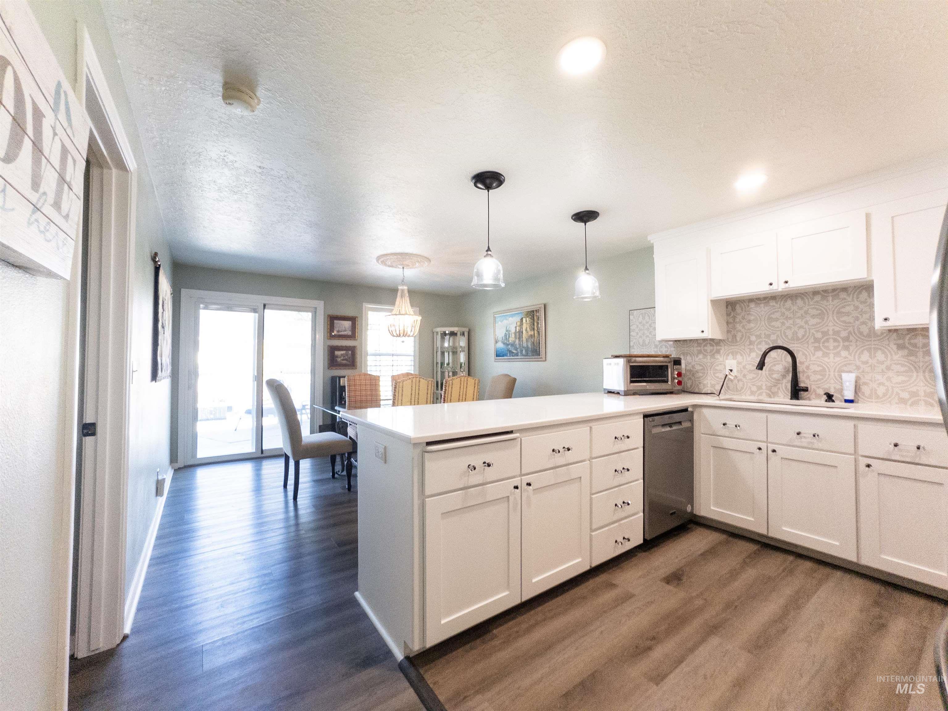 Kitchen featuring a textured ceiling, decorative backsplash, light countertops, a peninsula, and dark wood-style floors