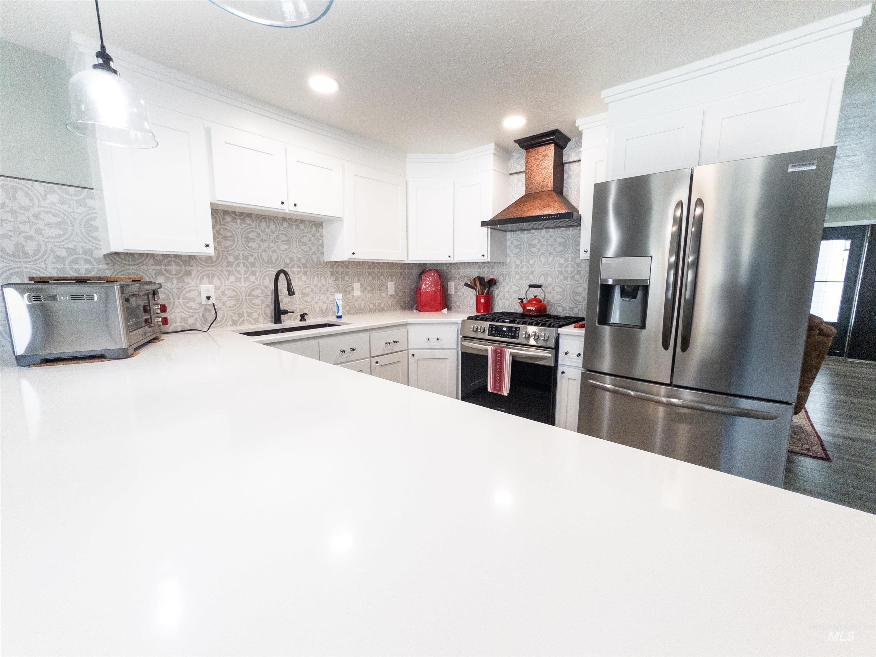 Kitchen with stainless steel appliances, backsplash, premium range hood, white cabinetry, and hanging light fixtures