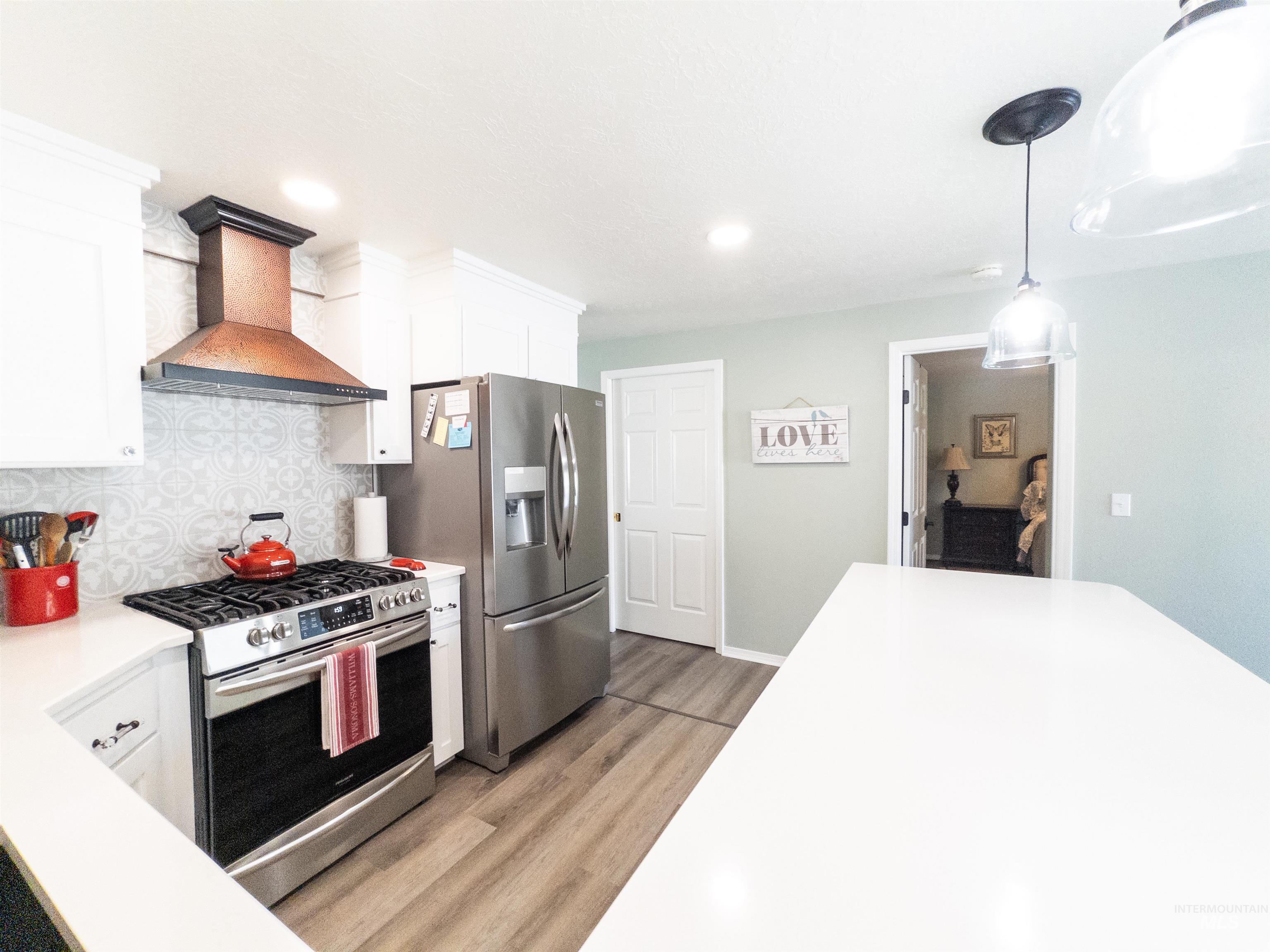 Kitchen with stainless steel appliances, white cabinetry, custom range hood, decorative backsplash, and light wood-type flooring