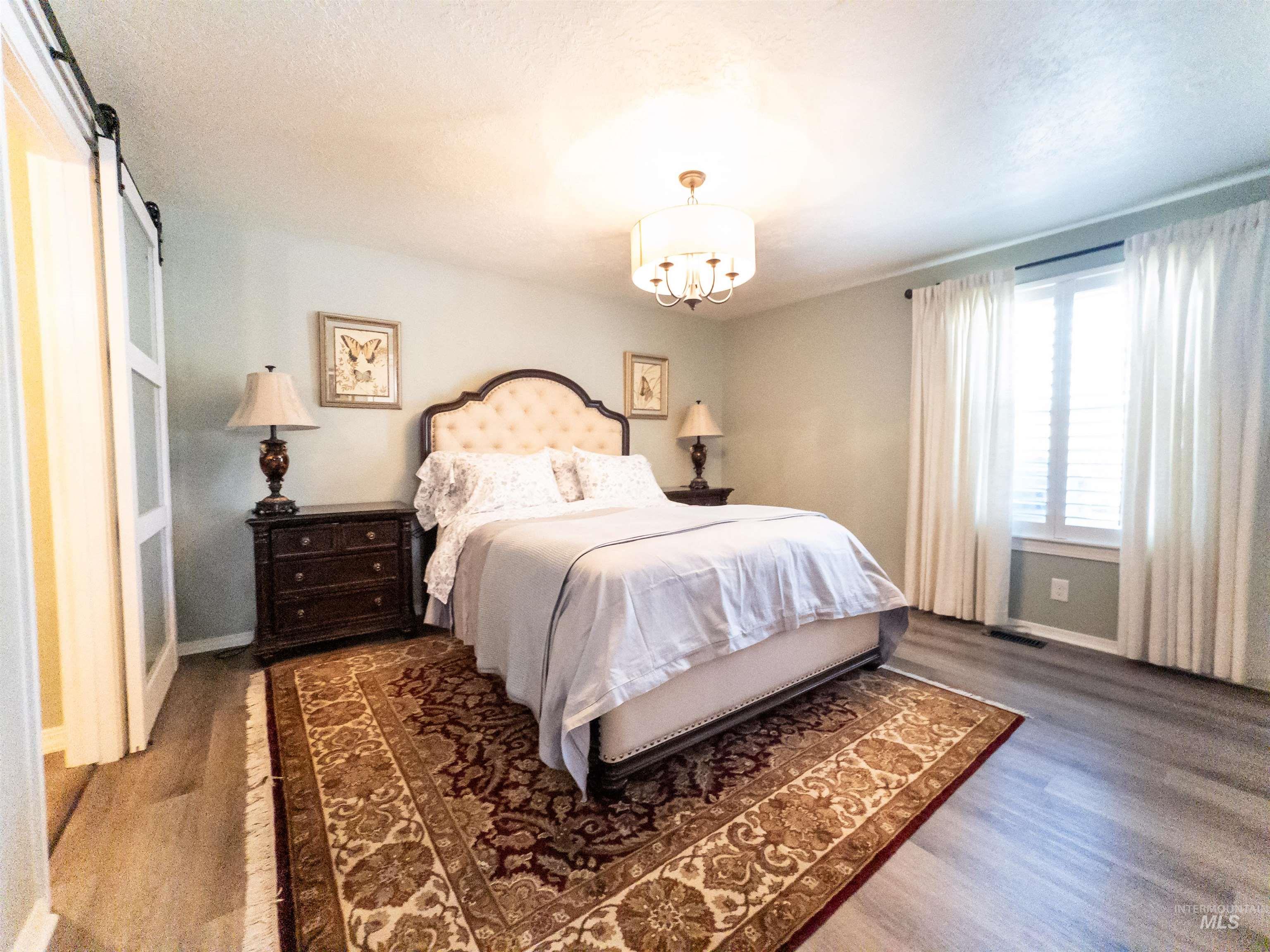Bedroom with wood finished floors, a barn door, and a chandelier
