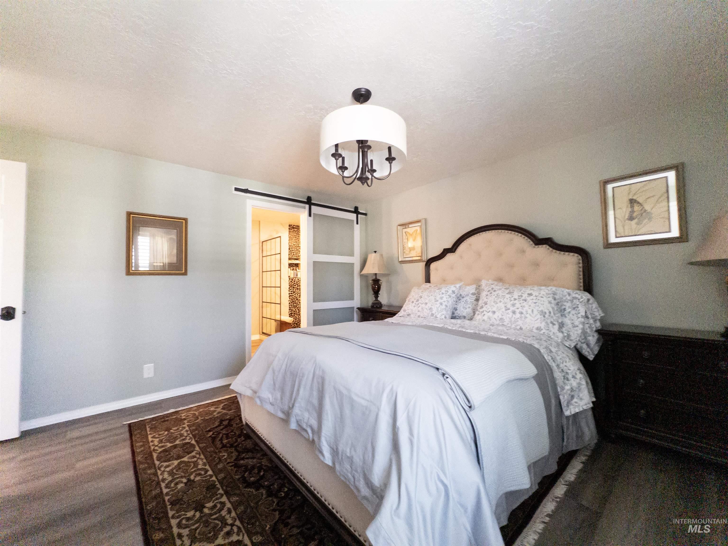 Bedroom with a barn door, a textured ceiling, dark wood finished floors, ensuite bath, and a chandelier