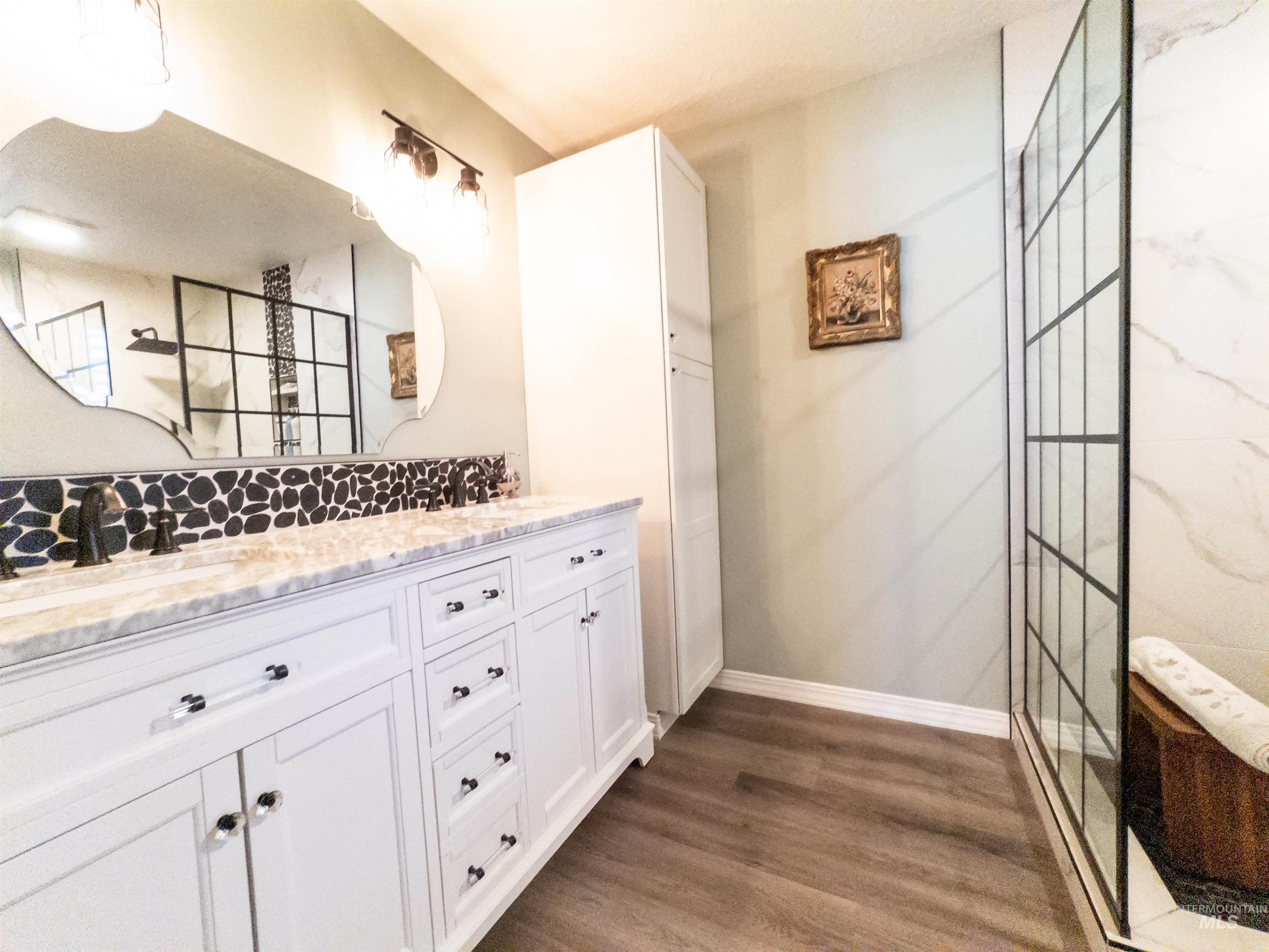 Bathroom featuring double vanity, dark wood finished floors, and a walk in shower