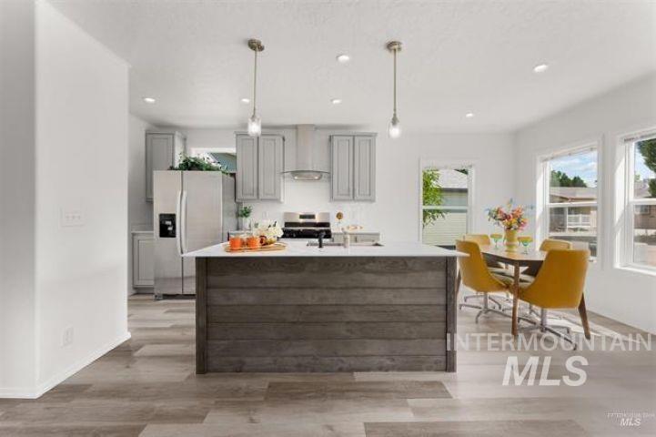 Kitchen with appliances with stainless steel finishes, gray cabinetry, an island with sink, premium range hood, and light wood-style floors