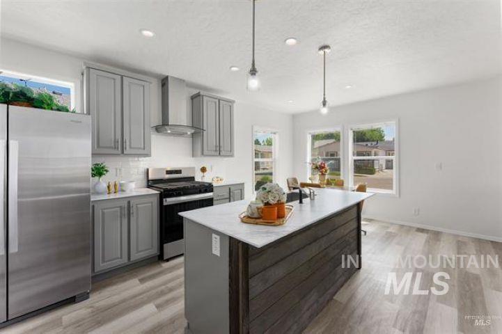 Kitchen featuring stainless steel appliances, wall chimney exhaust hood, plenty of natural light, a center island with sink, and a textured ceiling