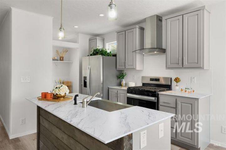 Kitchen featuring gray cabinets, stainless steel appliances, wall chimney range hood, and a kitchen island with sink