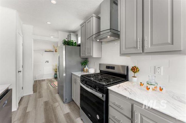Kitchen featuring appliances with stainless steel finishes, wall chimney range hood, gray cabinetry, light wood-type flooring, and decorative backsplash