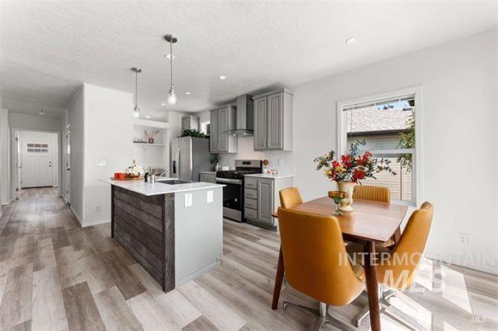 Kitchen featuring gray cabinetry, stainless steel appliances, light wood-style flooring, wall chimney range hood, and a textured ceiling