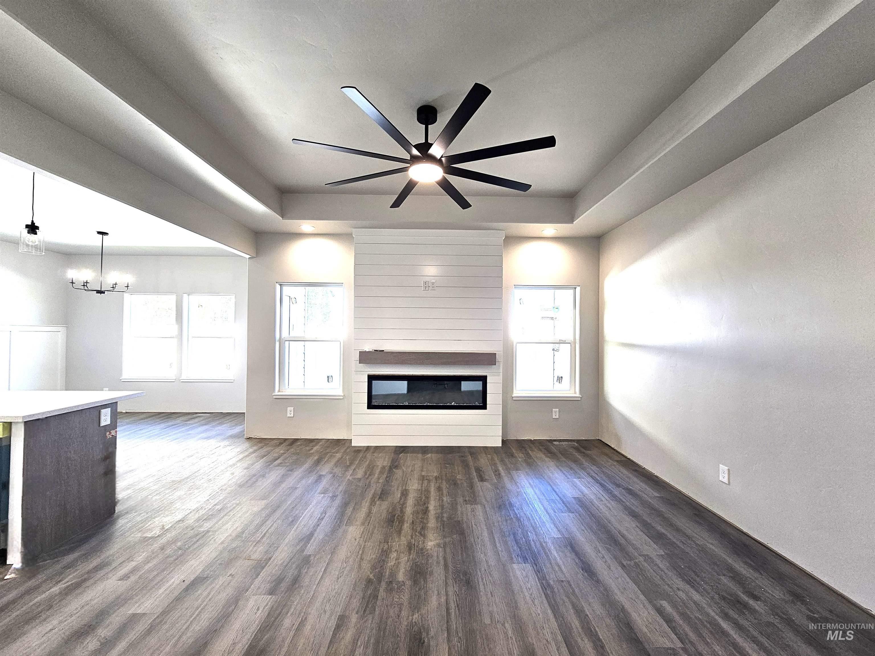 Unfurnished living room with a raised ceiling, dark wood-style floors, ceiling fan, and a fireplace