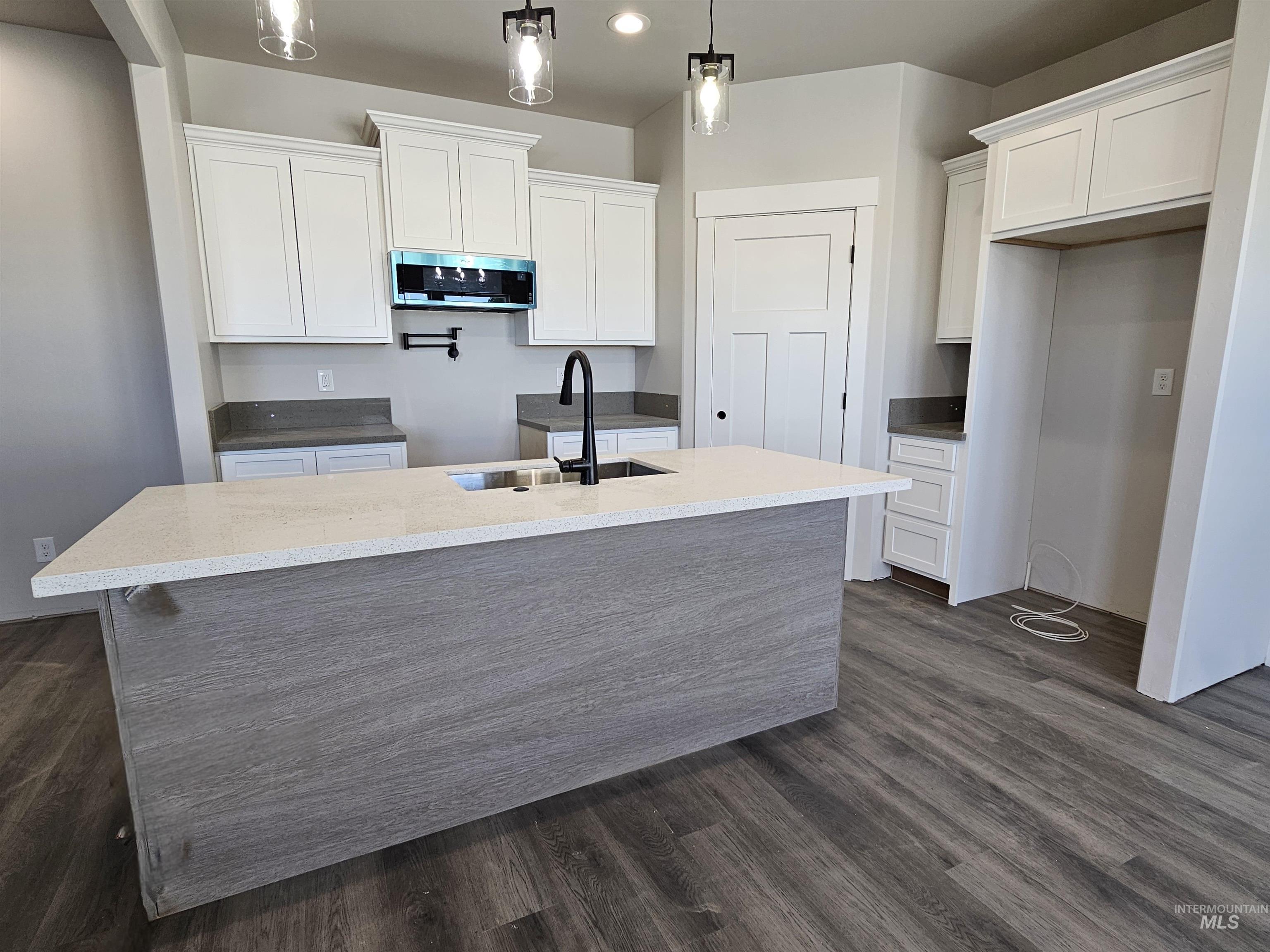 Kitchen with white cabinets, pendant lighting, dark wood-style floors, an island with sink, and light stone counters