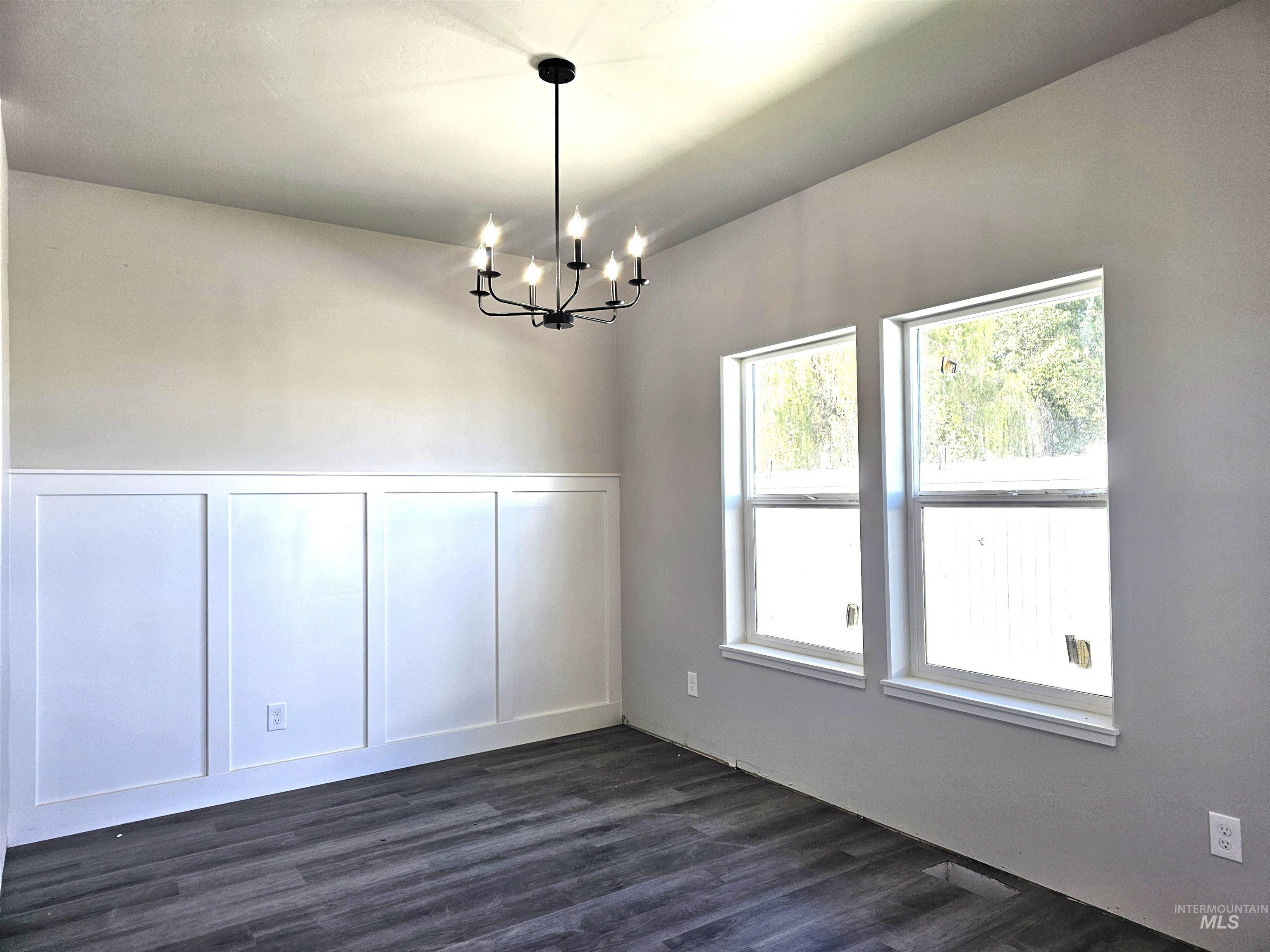 Unfurnished dining area featuring a decorative wall, a wainscoted wall, a chandelier, and dark wood-type flooring
