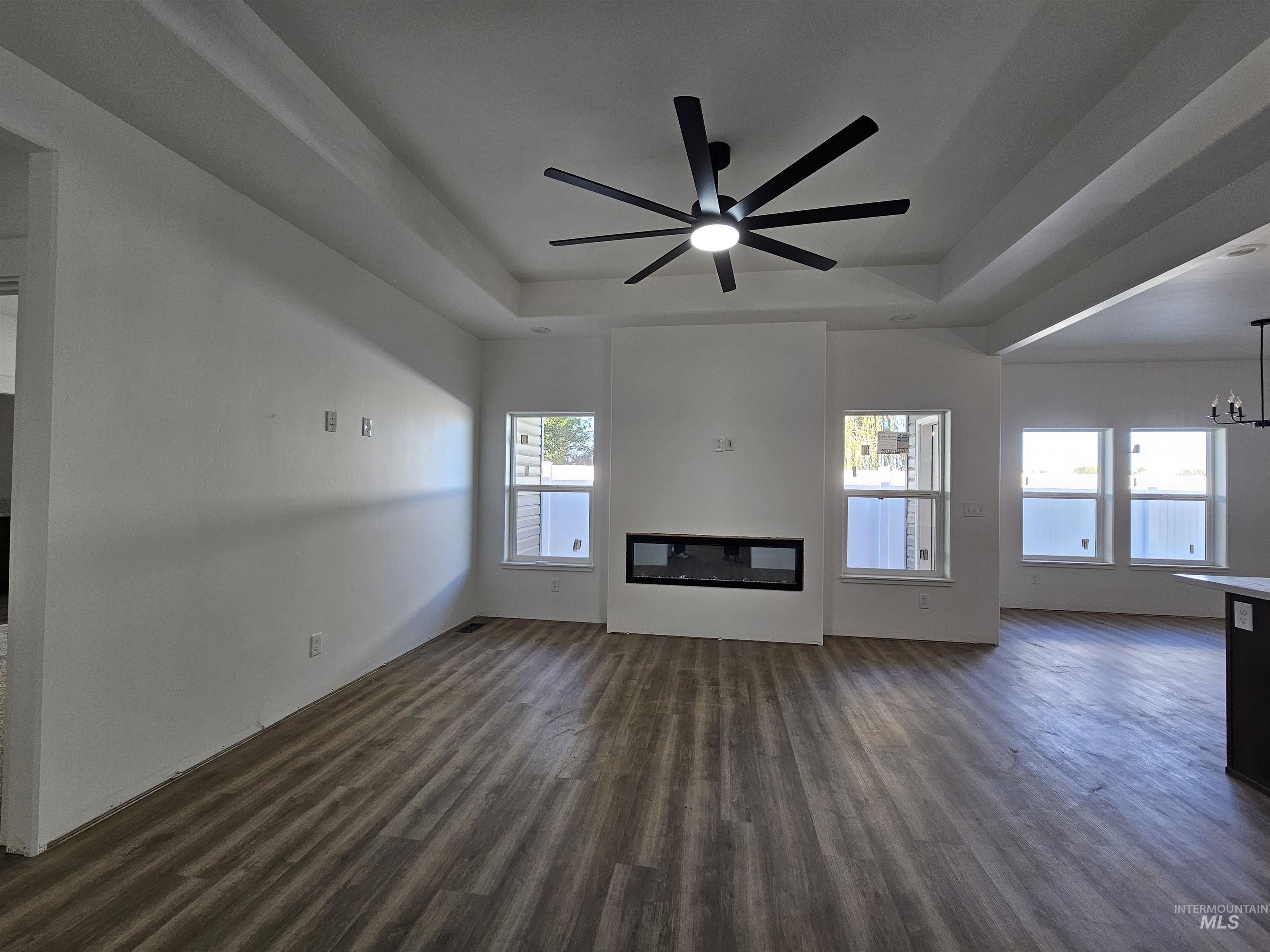 Unfurnished living room with a raised ceiling, dark wood finished floors, a ceiling fan, and a glass covered fireplace
