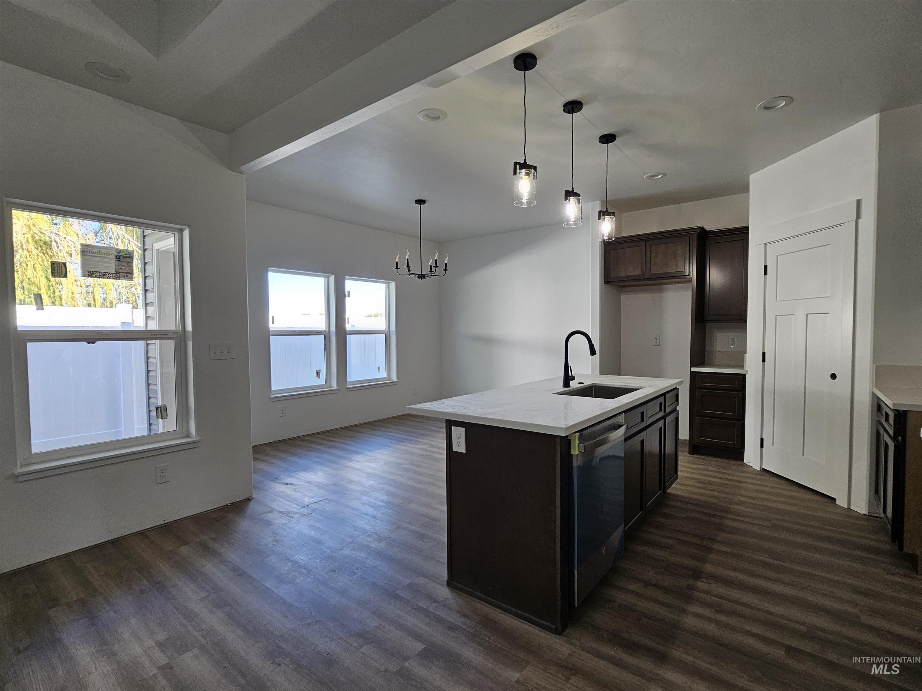 Kitchen featuring decorative light fixtures, a kitchen island with sink, dark wood-style floors, open floor plan, and dark brown cabinetry